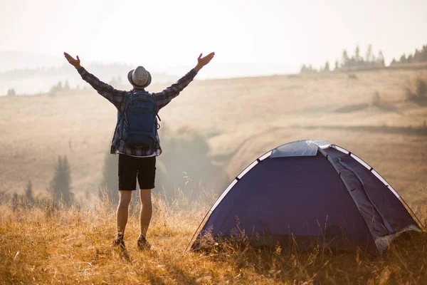 Silueta del hombre levantó las manos con la mochila en las vacaciones de camping al atardecer en la cima de las montañas — Foto de Stock