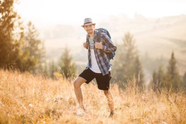 Sırt çantasıyla dağlar ormanında yürüyüş şapkalı sakallı turist. Beyaz erkek yürüyüşçü doğada açık havada.