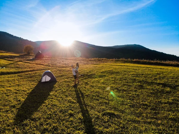 Vista de silueta aérea de figuras de tipo feliz sosteniendo a su novia mientras esta levanta los brazos al atardecer durante el campamento de montaña —  Fotos de Stock