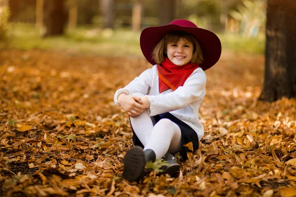 Gelukkige kleine kind meisje glimlach in hoed en herfst oranje bladeren. Outdoor. — Stockfoto