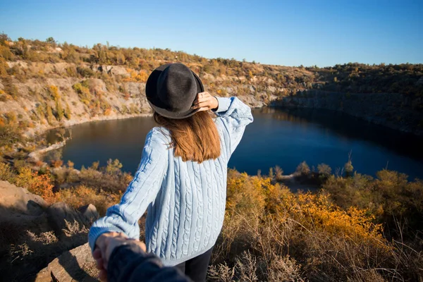 Tourist woman in black hat holding man by hand and go to lake in autumn mountains. Follow me concept — Stock Photo, Image