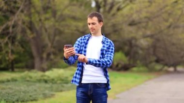 Genç adam selfie çekmek için telefon kullanıyor, parkta yürüyor ve fotoğraf ya da video için mobil uygulama kullanmaktan mutlu oluyor..