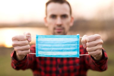 Elinde tıbbi maske olan güçlü bir adamın açık hava portresi. Koronavirüs salgınının sonu. Hastalık ve enfeksiyona karşı koruma.