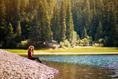 Hasır şapkalı turist kadın turkuaz mavi göl ve manzaranın yanında dinleniyor. Doğa, seyahat, macera, yürüyüş.