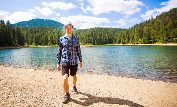 Man in hat walking outdoor Travel Lifestyle vacations concept with lake and mountains on background