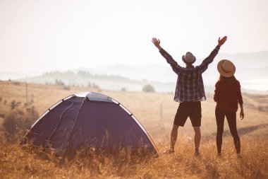 Sevgi dolu çiftin silueti sonbahar tatilinde kamp kurarak rahatlar. Moutain'in üstünde. Eller yukarı ile birlikte gün doğumunun tadını çıkarın.