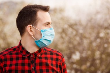 Yüz maskesi takan genç bir adamın portresi hava kirliliğinden korunuyor Coronavirus covid-19 çiçek açan ağacın yanında.