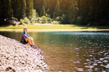 Turist genç adam yazın orman gölü sahilinde yürüyor. Tatil kavramı