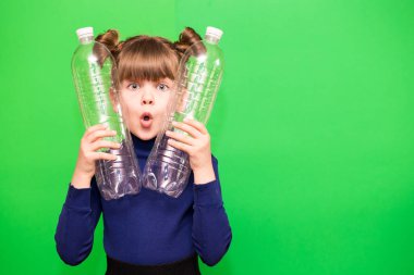 Kafası karışmış, elinde plastik şişelerle yeşil arka planda izole edilmiş küçük bir kızın fotoğrafı. ekoloji kavramı