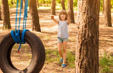Mutlu aktif kız çocuğu güneşli bir yaz gününde ormanda salıncakta sallanıyor. Çocuklar için yaz açık hava aktivitesi. Anaokulu çocuğu eğleniyor ve lastik üzerinde sallanıyor.