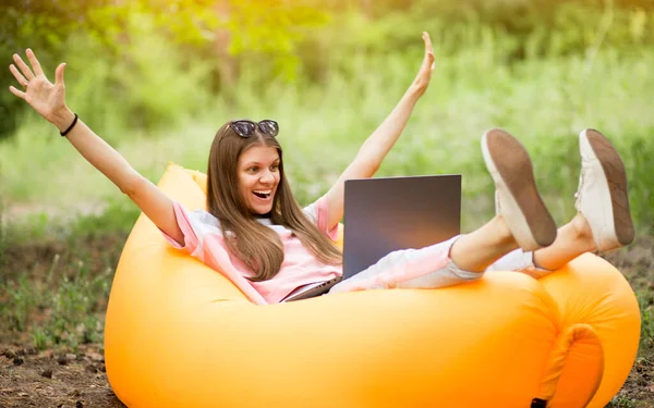 Elleri havada bir kadın, yaz parkında dizüstü bilgisayarla şişme kanepeye uzanmış mutluluk çığlıkları atıyor. Telework