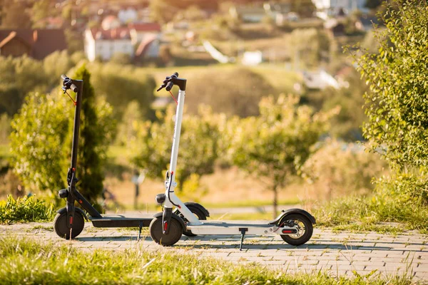 Sonbahar parkında iki yeni siyah-beyaz elektrikli scooter hazır bekliyor.