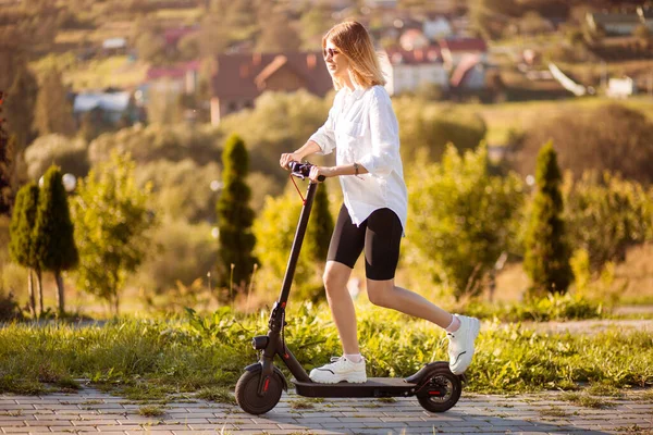 Genç ve şık bir kadın işe elektrikli scooterla gidiyor, modern kız, yeni nesil, elektrikli taşıma, ekolojik ulaşım