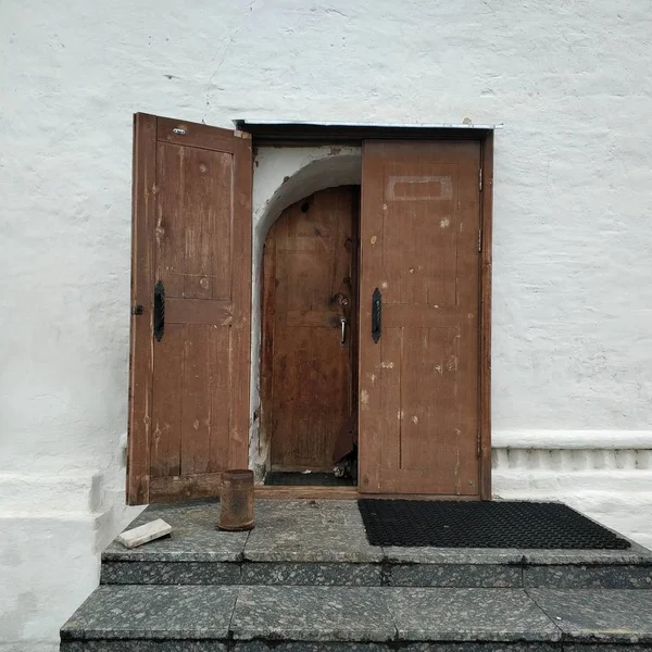 An open wooden old brown door on a white house. Element of the old church.