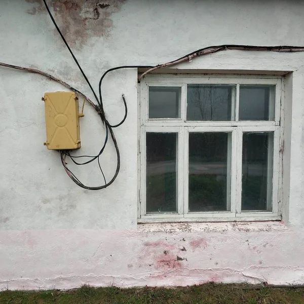 An old white building with a window and electrical wires.