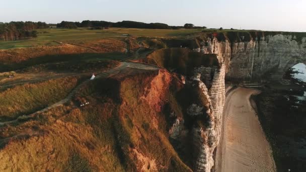 Schönes Drohnen-Selfie, glückliche junge Frischvermählte, die an der Steilküste der Normandie westlich über dem Ozean spazieren. toller Blick auf die Felsen von Etretat. Sonnenuntergang. Zeitlupe — Stockvideo