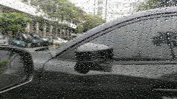 Rain drops on window with car background.