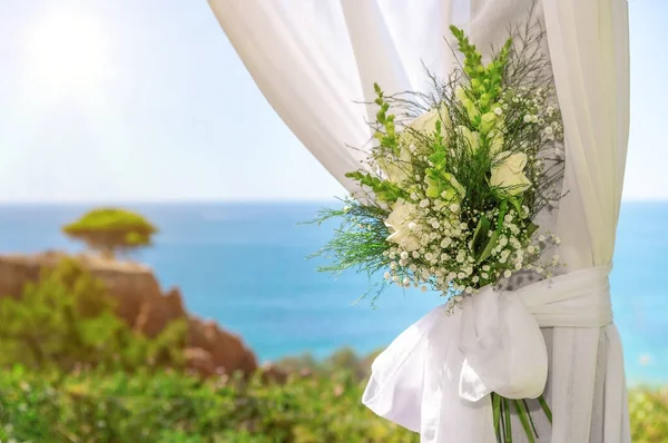 Krásná svatební kytice v tylu, svázaná stuhou, na pozadí oceánu a přírody za slunečného dne. Detailní záběr. — Stock fotografie