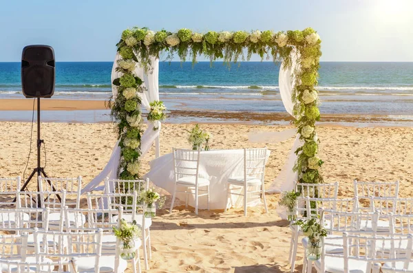 Romantyczna ceremonia ślubna nad oceanem, plaża w słoneczny dzień. Drewniany łuk ozdobiony świeżymi kwiatami. Białe fotele na piasku. — Zdjęcie stockowe