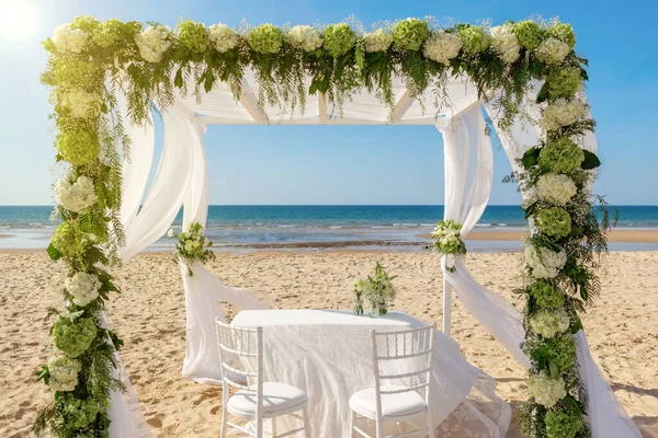 Lyxig romantisk bröllopsceremoni på havet, strand på en solig dag. Träbågen är dekorerad med färska blommor och vita tyll. — Stockfoto