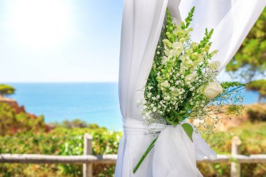Güneşli bir günde, okyanusun arka planına kurdeleyle bağlanmış, tül içinde güzel bir düğün buketi. Yakın plan..