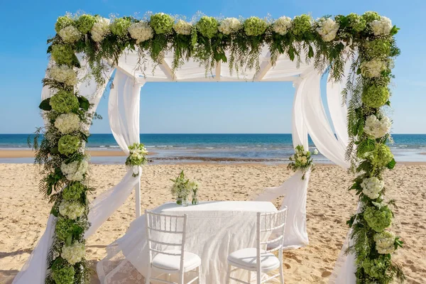 Lyxig romantisk bröllopsceremoni på havet, stranden. Träbågen är dekorerad med färska blommor och vita tyll. — Stockfoto