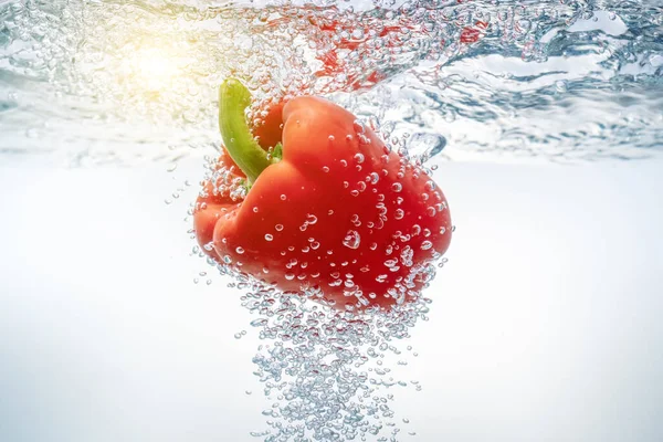 Vallende rode paprika 's in ecologisch schoon water waardoor de zon doorbreekt. Close-up. — Stockfoto