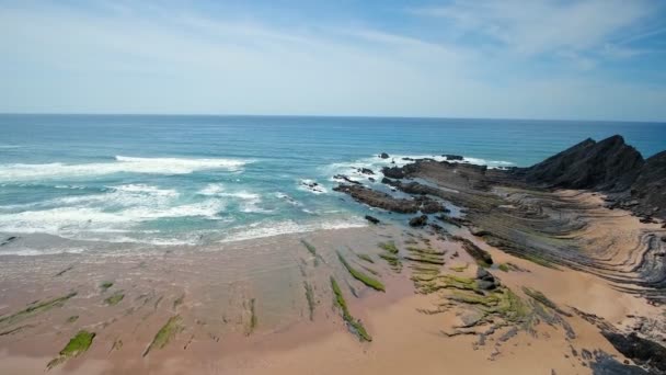 Natáčení leteckých videí. Vlny oceánu bušící do skal, kameny na pláži Arrifana, Sagres, Portugalsko, Algarve. Jasné modré nebe. — Stock video