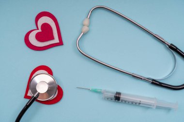 Tıbbi aletler steteskop, mavi arka planda kalbi olan şırıngalar..