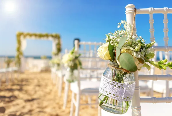 Luxuriöse Hochzeitszeremonie am Meer, Strand an einem sonnigen Tag. Weiße Stühle dekoriert mit einem schönen Blumenstrauß in einem Gefäß, das an ihnen hängt. — Stockfoto