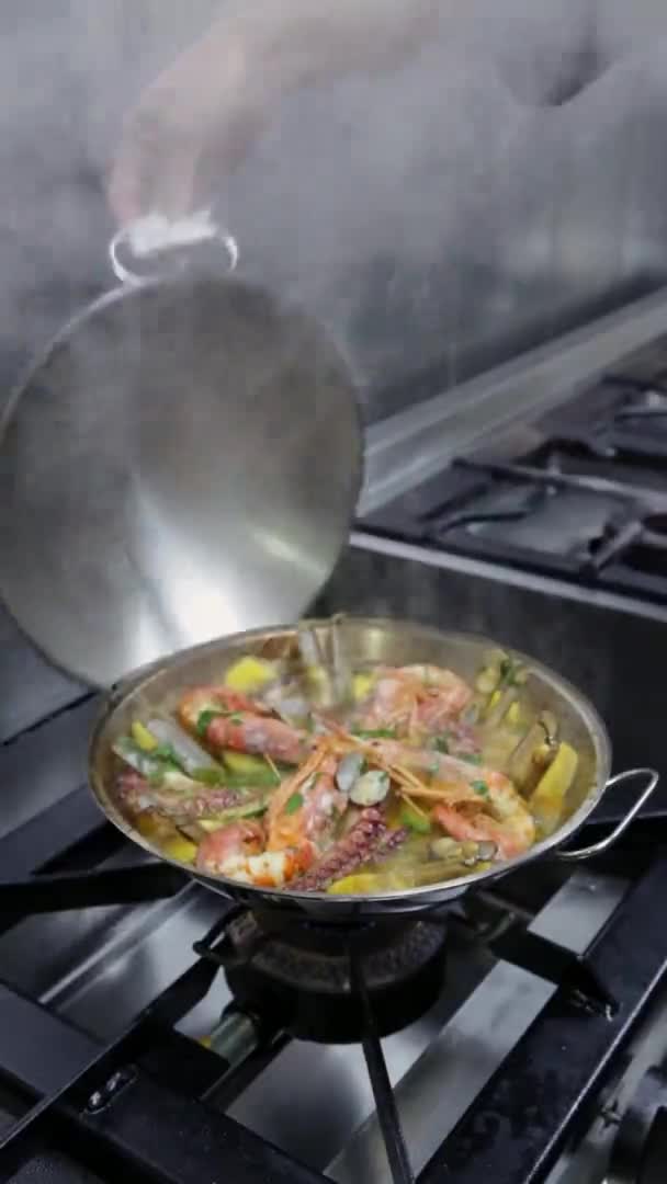 Ο σεφ αφαιρεί το καπάκι από το cataplan, το οποίο μαγειρεύει θαλασσινά και λαχανικά, σε μια κουζίνα αερίου. Κάθετο βίντεο. Κοντινό πλάνο. — Αρχείο Βίντεο