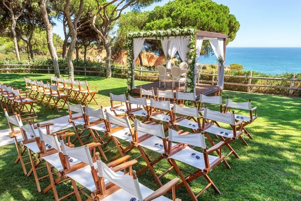 Piękny ślub nad oceanem. Zielony trawnik z łukiem z kwiatami i krzesłami na trawie. — Zdjęcie stockowe