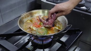 Şef ahtapot, deniz ürünleri ve sebzelerle mancınık pişiriyor. Yatay video. Yakın plan..