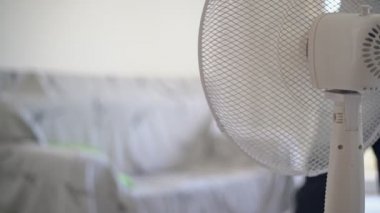 Havalandırma için elektrikli vantilatör. Elinde telefonla kanepede uzanan bir adam. Yakın plan..