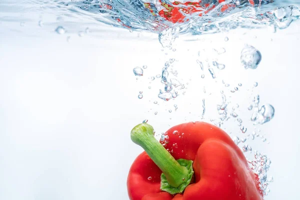 Ζουμερές κόκκινες πιπεριές στην επιφάνεια του οικολογικού καθαρού νερού, που πέφτουν, σχηματίζοντας βολβούς. Αντιγραφή χώρου. Κοντινό πλάνο. — Φωτογραφία Αρχείου