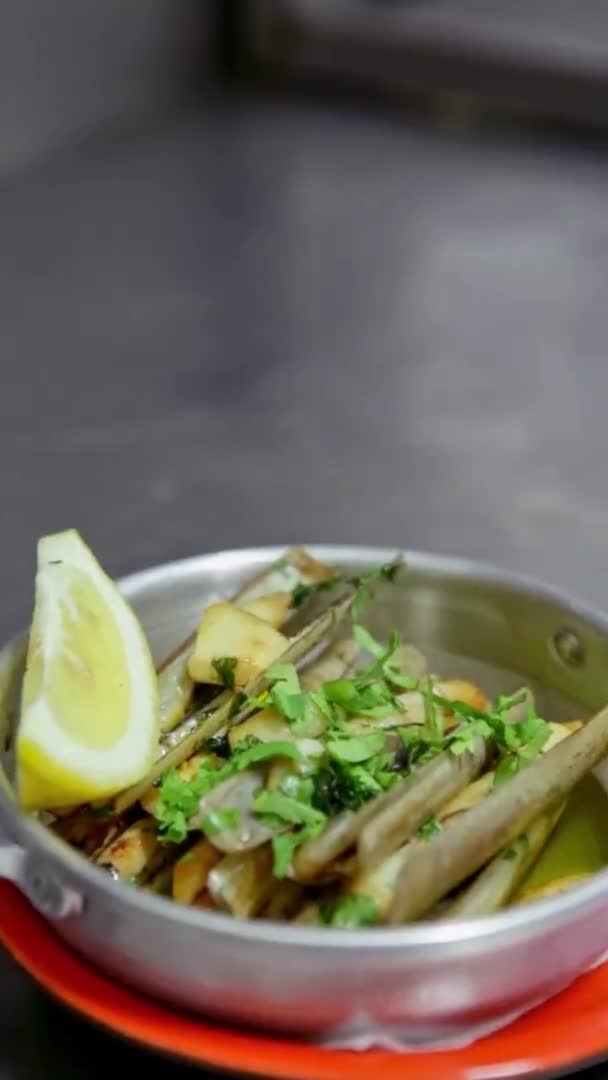 Almeja apetecible con ajo, hierbas, dispuestos en un plato de aluminio, decorado con una docena de limón. Vídeo vertical. Primer plano . — Vídeos de Stock