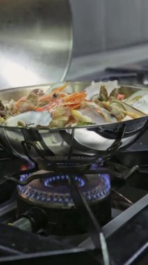 Şef, gaz sobasında pişirilen mancınığın kapağını açar. Dikey video. Yakın plan..