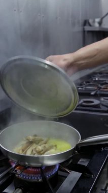 Şef bir istiridye pişirir tavada sarımsak ile, çok yüksek ısıda, bitmiş tabağa bitkisel otlar serpiştirir. Dikey video. Yakın plan..
