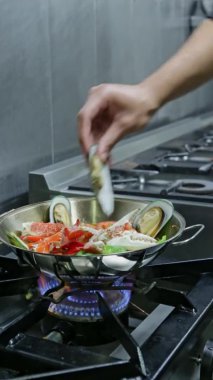 Şef, mancınığı ateşte, gaz sobasında pişiriyor. Dikey video. Yakın plan..