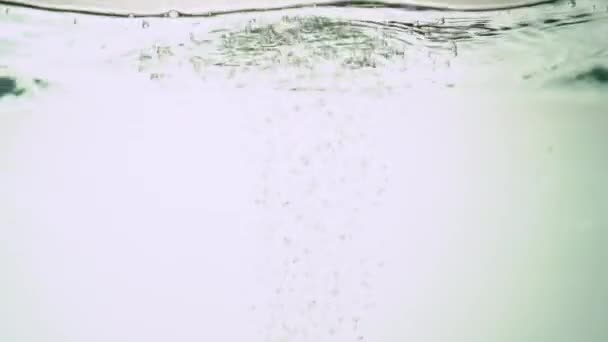 Ecologische rode peper wordt ondergedompeld in water, waardoor bubbels en waterschommelingen ontstaan. Op witte achtergrond. Close-up. — Stockvideo