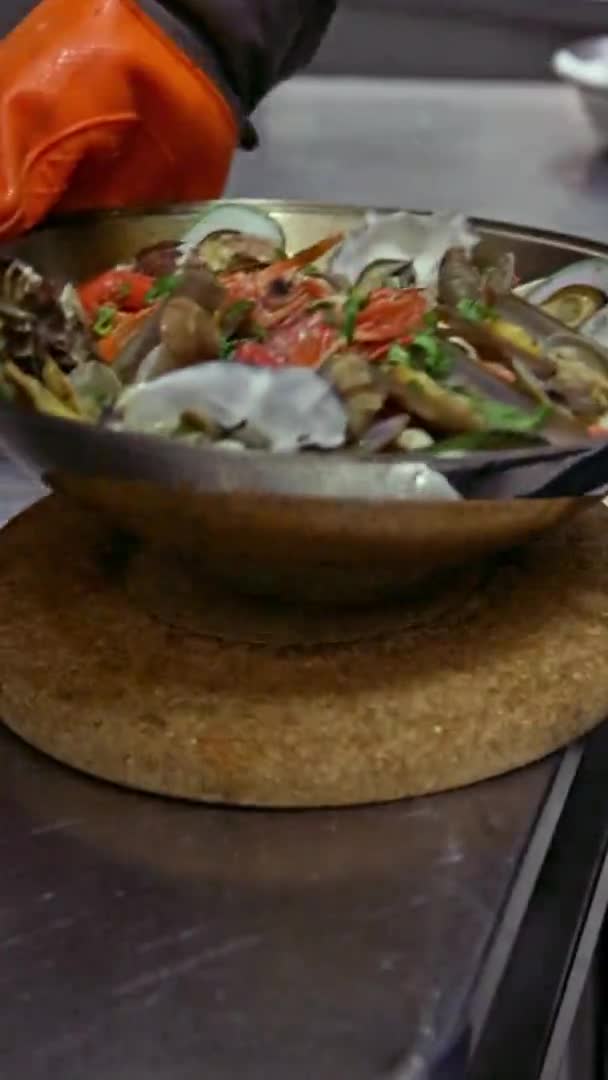 El chef pone sobre la mesa un cataplan cocinado con pulpo, mariscos, verduras y batatas. Vídeo vertical. Primer plano . — Vídeos de Stock