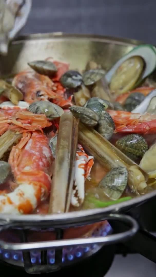 Koch kocht einen Kataplan, ein portugiesisches Gericht, mit Meeresfrüchten in Flammen, auf einem Gasherd. Vertikales Video. Nahaufnahme. — Stockvideo