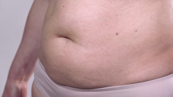 Une femme d'âge moyen à la peau affaissée définit son gros ventre avec un ruban à mesurer, sur un fond blanc. Plan latéral. — Video
