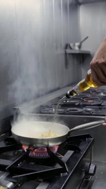Aşçı, güçlü alevlerin olduğu bir tavada, kalamar kızartması. Dikey video. Kapat..