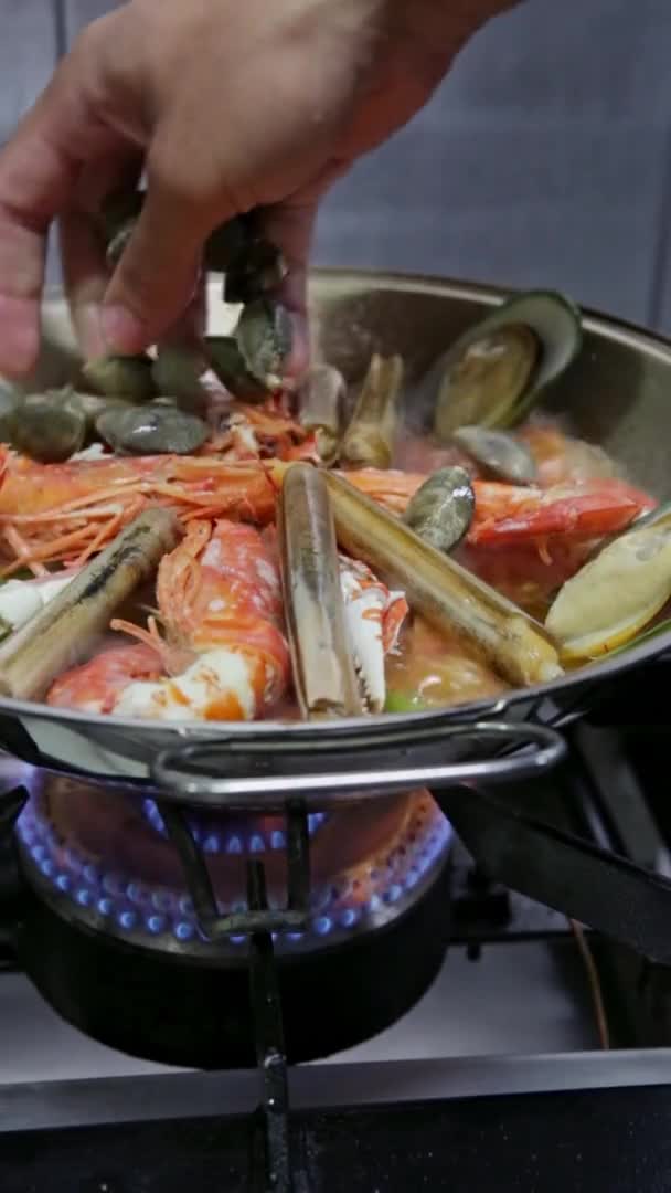 Koch kocht einen Kataplan, ein portugiesisches Gericht, mit Meeresfrüchten in Flammen, auf einem Gasherd. Vertikales Video. Nahaufnahme. — Stockvideo