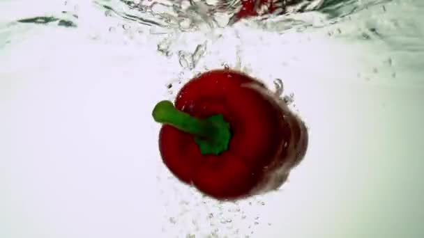 Eco-friendly red pepper is immersed in water, creating bubbles and water swings. On white background. — Stock Video