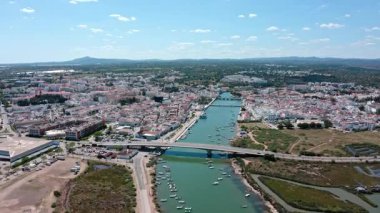 Gilao nehri, yol köprüsü, tekneler, binalar ve Portekiz 'in çevresindeki manzara ile Tavira şehir merkezinin güzel hava manzarası. Tavira Portekiz 15.06.2025