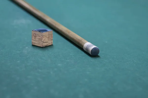 A cue stick and a chalk on a pool table.