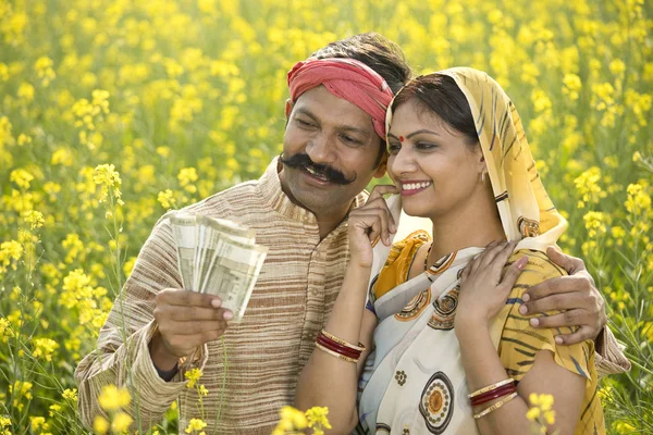 Rural couple holding Indian rupee notes in agriculture field