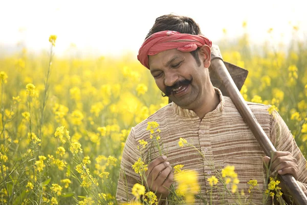 stock image Portrait of happy farmer holding hoe in rapeseed field